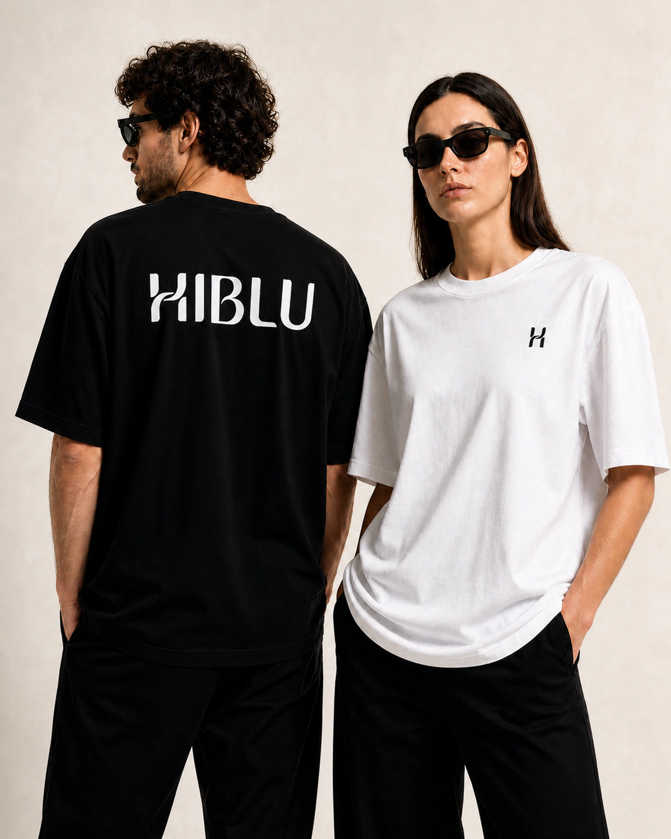 A male model wearing a black HIBLU wordmark T-shirt shown from the back beside a female model wearing a white T-shirt with the HIBLU symbol